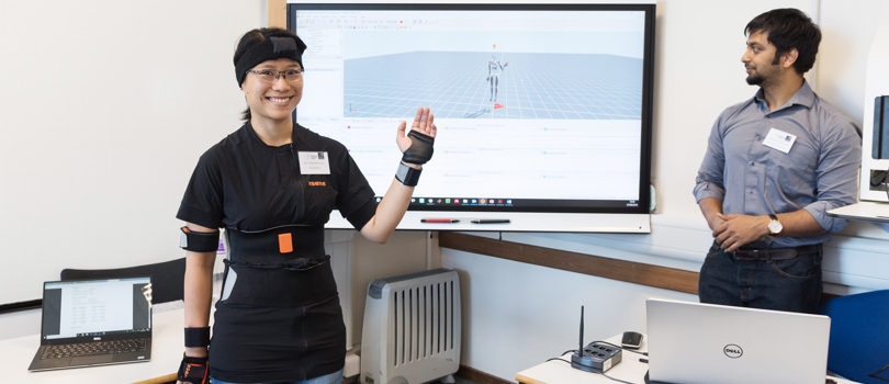 Woman demonstrating a gadget reflecting her actions on a screen behind her.