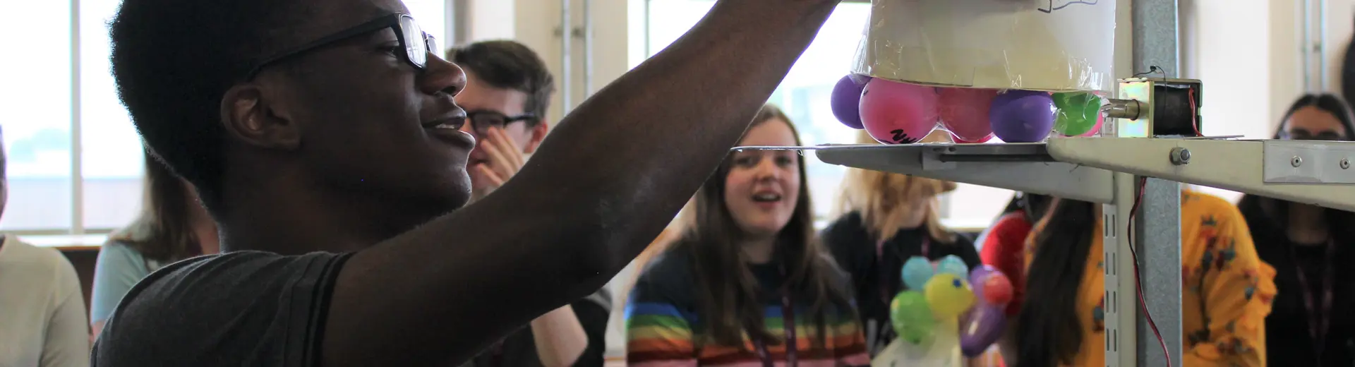 Student placing balloon project on scales infront of classmates