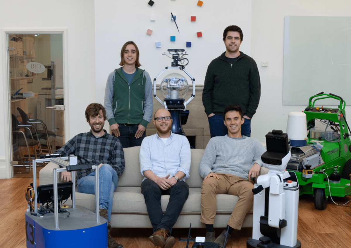 GOALS group photo sitting on lounge with robots in front.