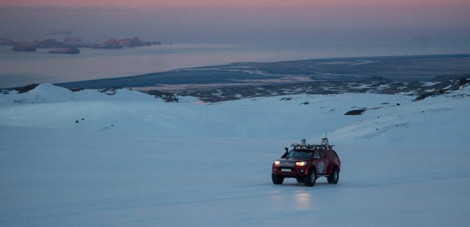 Red vehicle on glacier at sunset in Iceland. 