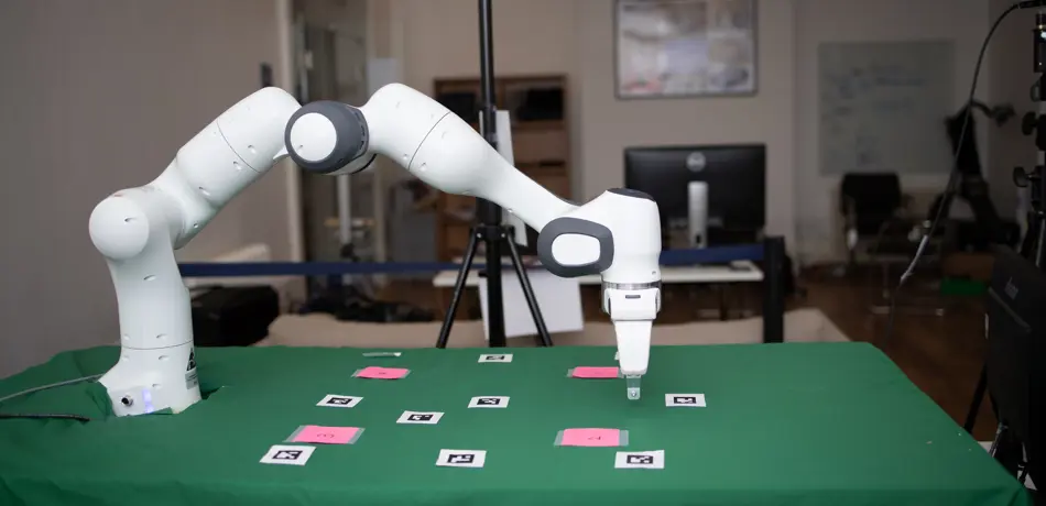 Panda robot arm picking up cards on green table.
