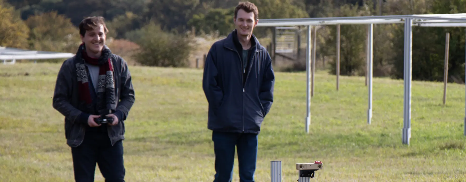 Two men walking with a robot in a solar farm.