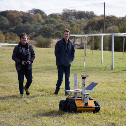 Two men walking with a robot in a solar farm. 
