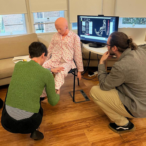 An OT and a researcher move a mannequin's leg to get the robotic feedback from the sensors and software.